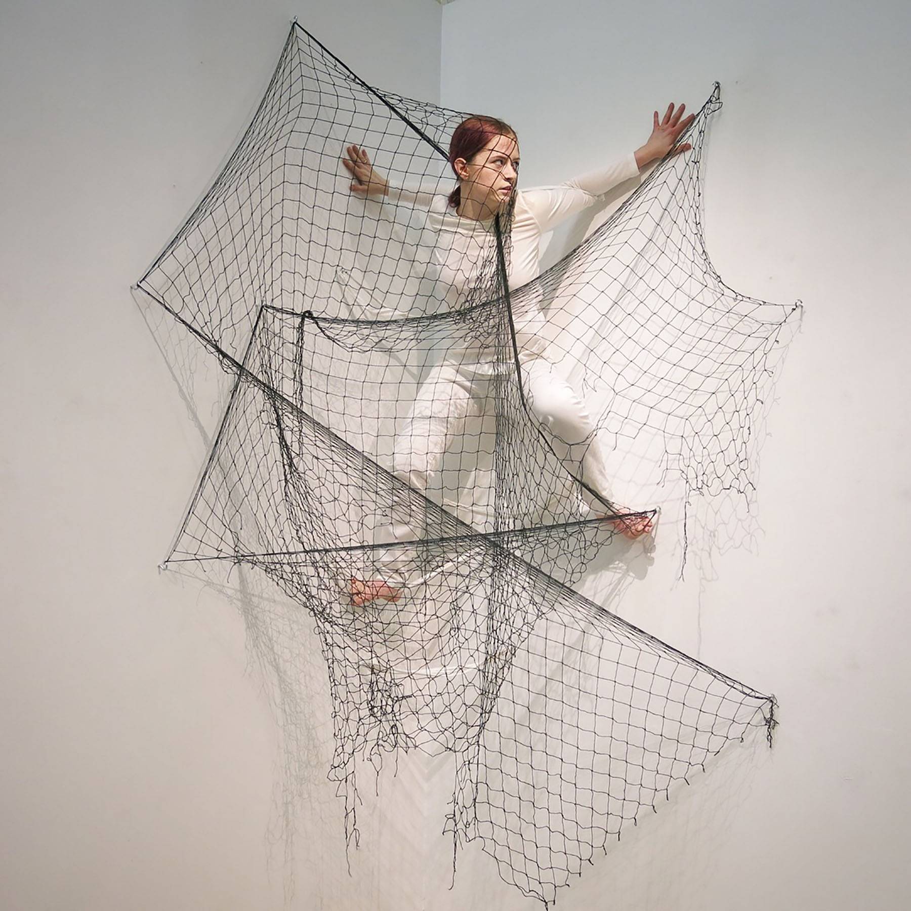 girl floating with her back to a white wall surrounded by a black net